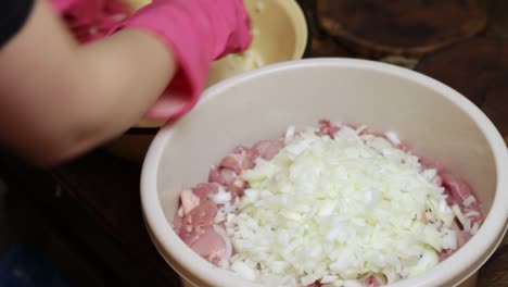 Gloved-hands-adding-chopped-white-onions-into-a-bowl-of-raw-chicken-for-shashlik