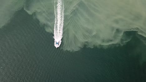 Top-View-Of-A-Powerboat-Sailing-On-The-Shallow-Blue-Sea-With-Silt-Sand-On-The-Sea-Bed---aerial
