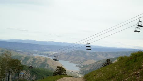 Beautiful-scenic-tilt-up-shot-of-Deer-Creek-lake-on-rolling-rocky-mountain-hills-from-the-top-of-Sundance-Ski-Resort-with-ski-lifts-passing-up-and-down-on-a-warm-summer-sunny-day-in-Utah,-USA
