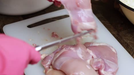 Person-wearing-rubber-gloves-slicing-raw-chicken-breast-with-a-sharp-knife