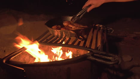 Camping-trip-evening-barbecue-over-fire,-chicken-drumsticks-in-pan