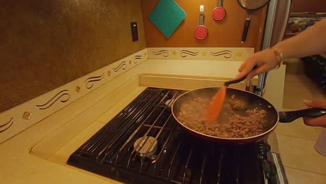 Woman-cooking-ground-meat-with-onions-in-skillet-in-RV-kitchen