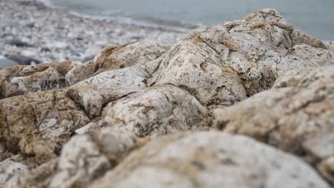 Rocky-pebble-stone-shoreline-with-ocean-waves-background-marine-landscape-close-up-right-dolly