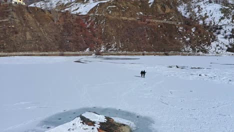 Couple-Holding-Hands-While-Walking-In-The-Frozen-And-Snow-covered-Lake-At-Winter-In-Sissu,-Himachal-Pradesh,-India