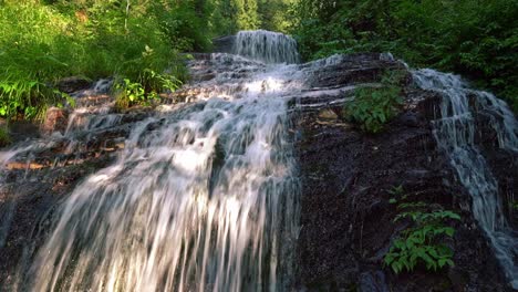 Schnell-Fließende-Wasserfälle-Von-Den-Felsigen-Klippen-Am-Wald-Mit-Einem-Sonnenstrahl-Im-Sommer