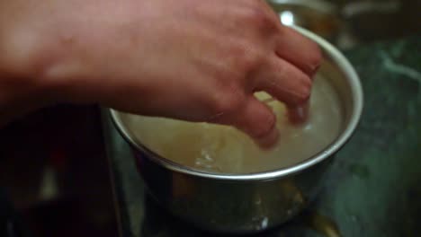 Reiskörner-Vor-Dem-Kochen-In-Einem-Kleinen-Topf-Mit-Wasser-Von-Hand-Reinigen