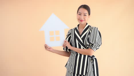 Successful-asian-real-estate-agent-and-businesswoman-showing-house-symbol,-full-frame-slow-motion,-isolated-on-beige-background