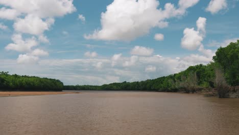Hyperlapse-shot-from-a-small-boat-sailing-on-the-muddy-tropical-river-in-Africa-with-beautiful-clouds,-blue-sky-and-fresh-green-trees-on-hot-summer-day