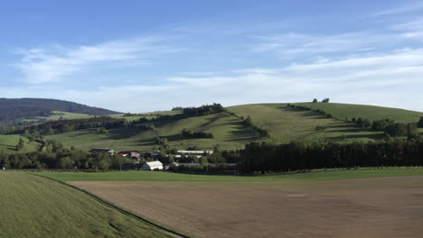 4K-Pan-Luftaufnahme-Eines-Kleinen-Dorfes-Im-Sommer-Inmitten-Einer-Grasbewachsenen-Landschaft-In-Dolní-Morava,-Tschechische-Republik,-Unter-Einem-Hügel-Mit-Bäumen-Und-Einem-Blauen-Himmel-Darüber