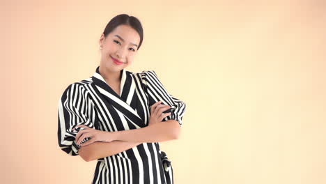 Hübsche-Stilvolle-Asiatische-Geschäftsfrau,-Die-In-Die-Kamera-Lächelt-Und-Ihre-Hände-Kreuzt,-Vollbild-Zeitlupe,-Einzeln-Auf-Beigem-Hintergrund
