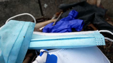 Dirty-disposable-corona-virus-face-masks-and-latex-gloves-among-cigarette-rubbish-on-street-curb-pull-back-closeup
