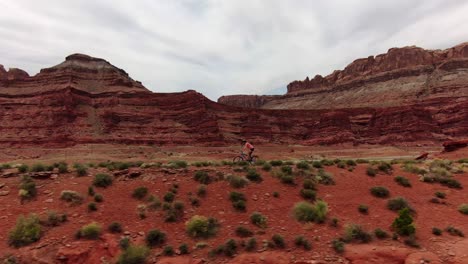 Aerial-shot-tracking-left-of-mountain-biker-cycling-along-flat-trail-in-red-Moab-desert