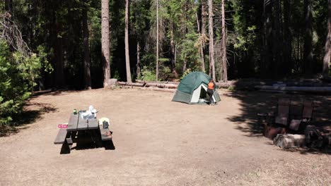 Low-aerial-dolly-shot-towards-camper-exiting-tent-in-campsite
