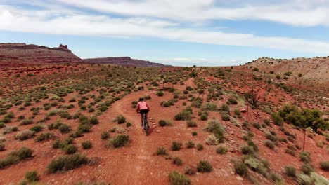 Aerial-shot-following-woman-riding-mountain-bike-along-beautiful-remote-Moab-trail