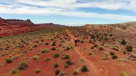 Aerial-shot-following-behind-woman-mountain-biking-along-Moab-desert-trail