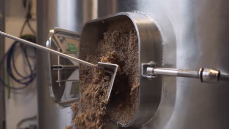 Pulling-Out-Spent-Grains-Of-Malt-From-The-Tank-With-A-Stainless-Scraper-In-The-Brewery---close-up-slowmo