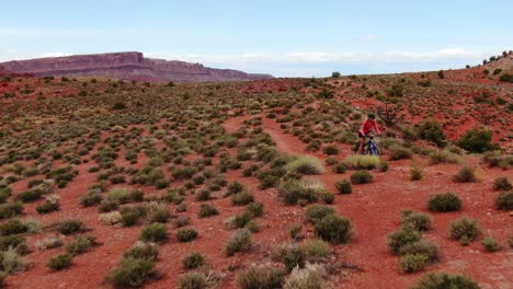 Aerial-dolly-backward-shot-of-mountain-biker-towards-camera-in-red-Moab-desert