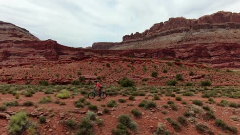 Aerial-tracking-shot-of-mountain-biker-following-flat-trail-in-red-Moab-desert