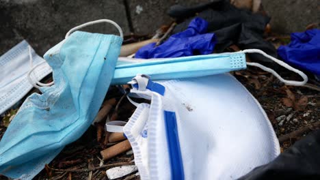 Dirty-disposable-corona-virus-face-masks-and-latex-gloves-among-cigarette-rubbish-on-street-curb-closeup-push-in