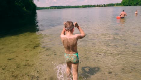 Happy-child-boy-sand-on-his-body-walking-towards-the-lake-water-to-swim