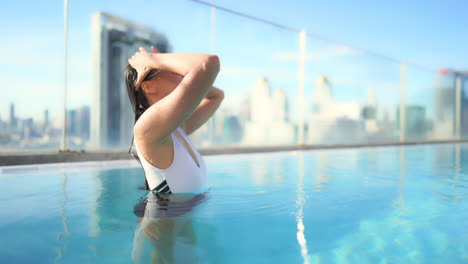 After-taking-a-dip-in-a-rooftop-resort-swimming-pool,-A-beautiful,-healthy,-fit-woman-brushes-her-wet-hair-away-from-her-face