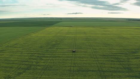 Spectacular-scenic-aerial-view-of-vast-flat-green-farmland-with-single-farming-machine-spraying-fungicide-on-crops,-Saskatchewan,-Canada,-high-aerial-pull-back