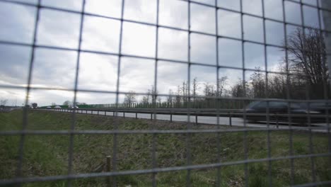 View-From-The-Steel-Fence-Of-Trucks-And-Cars-Passing-By-On-The-Road-In-Zlotoryja,-Poland-On-A-Cloudy-Weather---panning-shot