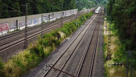 Un-Tren-Blanco-Pasa-Por-Debajo-De-Una-Serie-De-Líneas-Eléctricas-En-Un-Sistema-Ferroviario-De-Cuatro-Vías