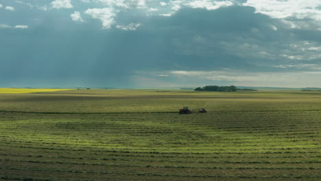 Sensationelles-Sonnenlicht-Und-Lichtstrahlen-Scheinen-Auf-Grünem-Ackerland-Mit-Traktor,-Der-An-Bewölkten-Tagen-Auf-Flachem-Ackerland-In-Weiten-Landschaften-Fährt,-Saskatchewan,-Kanada,-über-Der-Antenne-Seitlich