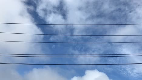 Weiße-Wolken,-Die-Sich-Tagsüber-In-Auckland,-Neuseeland,-Sanft-Am-Himmel-über-Stromleitungen-Bewegen