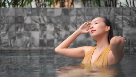 Beautiful-Asian-Woman-Relaxing-in-Swimming-Pool,-Fixing-Her-Wet-Hair,-Close-Up-Slow-Motion