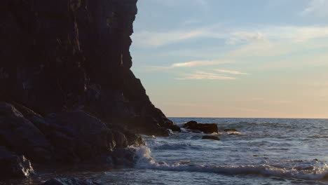 Waves-crash-against-cliff-rocks-in-golden-hour,-slow-motion