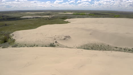 Dry-arid-desert-sand-dunes-in-expansive-flat-plains-landscape-on-sunny-blue-sky-day,-Sandhills,-Saskatchewan,-Canada,-overhead-aerial-pull-back