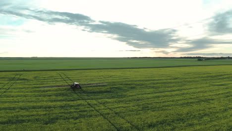 Vista-Aérea-Escénica-De-Tierras-De-Cultivo-Verdes-Y-Planas-Expansivas-Con-Maquinaria-Agrícola-Rociando-Fungicida-En-Cultivos,-Saskatchewan,-Canadá,-Por-Encima-De-La-Retirada-De-Drones