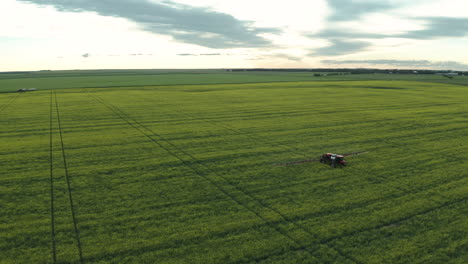 Tractor-spraying-fungicide-in-green-field,-tracking-drone-shot