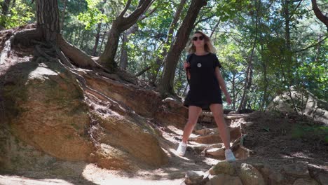 female-hiker-backpacker-wearing-black-clothes-walking-down-the-rocky-slope-hill-In-Gwanaksan-Mountain-forest-In-South-Korea-on-sunny-summer-day---from-view-low-angle