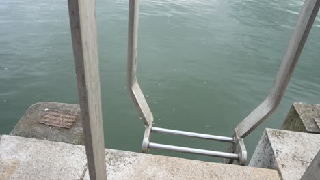 Steel-marina-ladder-leading-to-idyllic-ocean-water-reflections-waterfront-slow-pull-back