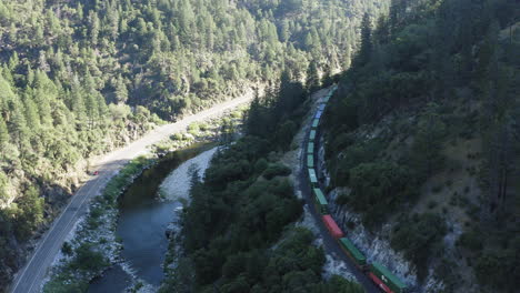 Aerial-of-a-valley-with-Union-Pacific-Railroad-passing-through,-big-cargo-train-traveling-through-gorge,-following-drone-shot