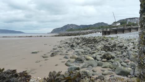 Sandy-stone-pebble-beach-with-mountains-overlooking-British-coastline-seaside-tourist-attraction-dolly-left