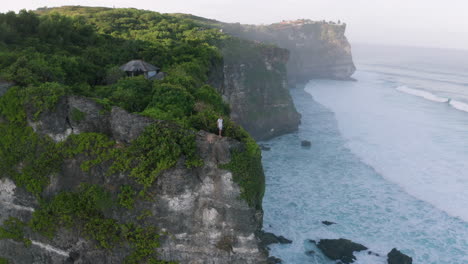 Man-stands-at-steep-cliff-edge-overlooking-ocean