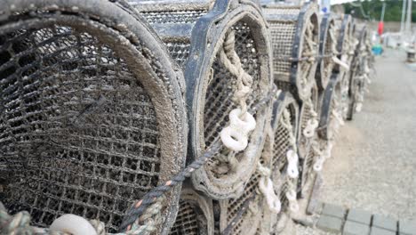 Fishing-harbour-group-of-stacked-lobster-pots-on-coastal-marine-waterfront-dolly-left-close-up