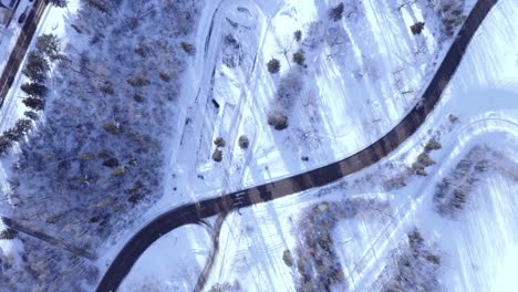 Aerial-zoom-in-survey-over-snow-covered-curvy-highway-freeway-inbetween-a-park-with-light-traffic-on-beautiful-winter-day-overlooking-a-frozen-residential-area-by-the-road-2-2