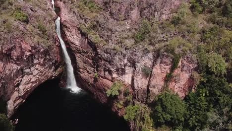 Flying-over-tall-waterfall-off-rocky-cliff-face-into-gorge