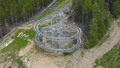 Aerial-4k-shot-of-a-huge-roller-coaster-loop-of-an-extreme-outdoor-ride-in-the-mountains-of-Dolní-Morava,-Czech-Republic,-standing-on-a-slope-with-trees-around