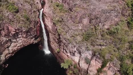 Drone-footage-of-waterfall-flowing-off-cliff-edge-into-large-lake