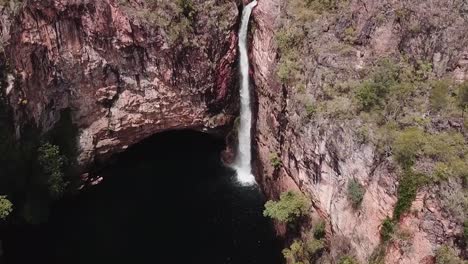 Drone-footage-over-tall-waterfall-flowing-off-cliff-face-into-large-canyon