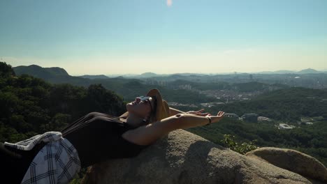 Caucasian-Girl-Wearing-A-Sunglasses-Ang-Looking-At-The-Beautiful-Sky-While-Lying-On-The-Rocks-At-The-Peak-Of-Gwanaksan-Mountain-In-Seoul,-South-Korea