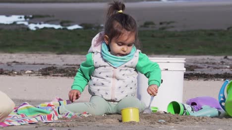 little-child-playing-with-a-spoon-and-colour-toys-on-the-beach,-Slowmo