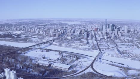 super-high-aerial-pan-out-of-winter-snow-covered-city-with-gradaitions-blue-clear-sky-of-a-curvy-horizon-with-bridges-connecting-to-the-downtown-core-crossing-icy-snow-covered-rivers-parks-forests