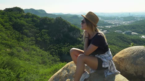 Chica-Elegante-Sentada-En-Las-Rocas-Y-Disfrutando-Del-Exuberante-Bosque-Junto-A-La-Montaña-Gwanaksan-En-Un-Día-Soleado-De-Verano-En-Seúl,-Corea-Del-Sur